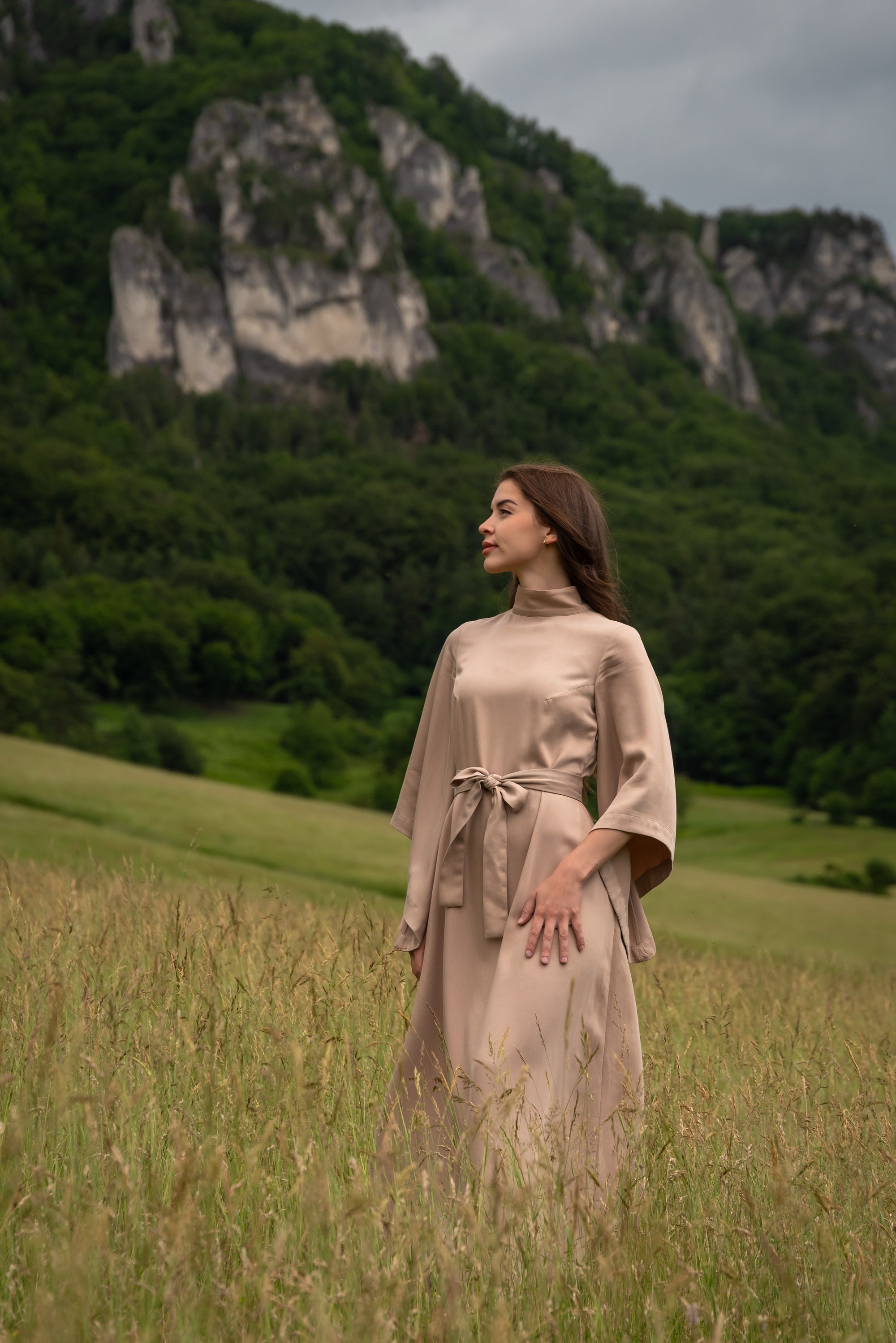 Woman in a beige dress standing in a field with mountains in the background