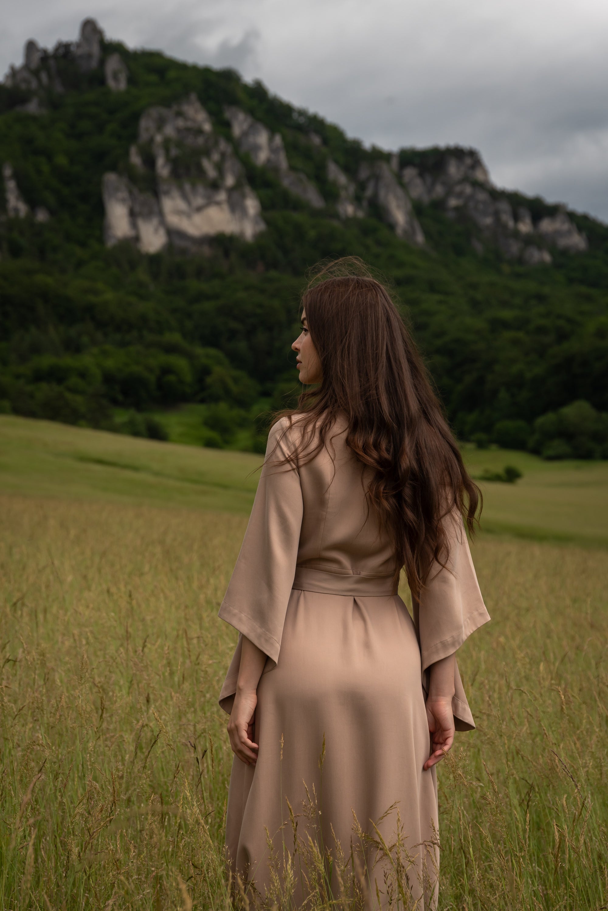 Woman in a beige dress standing in a field with mountains in the background